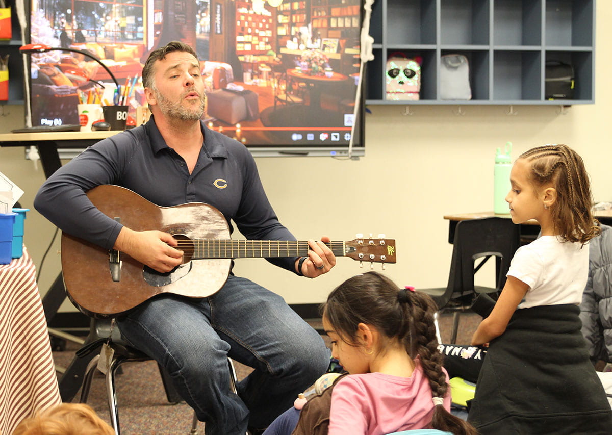 Counselor at Anderson Mill Elementary playing guitar and singing to students