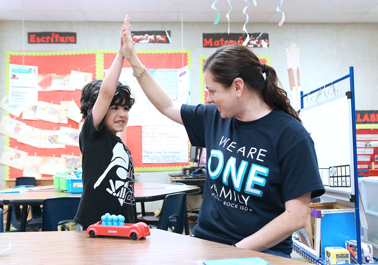 prekindergarten student and teacher doing a "high-five"